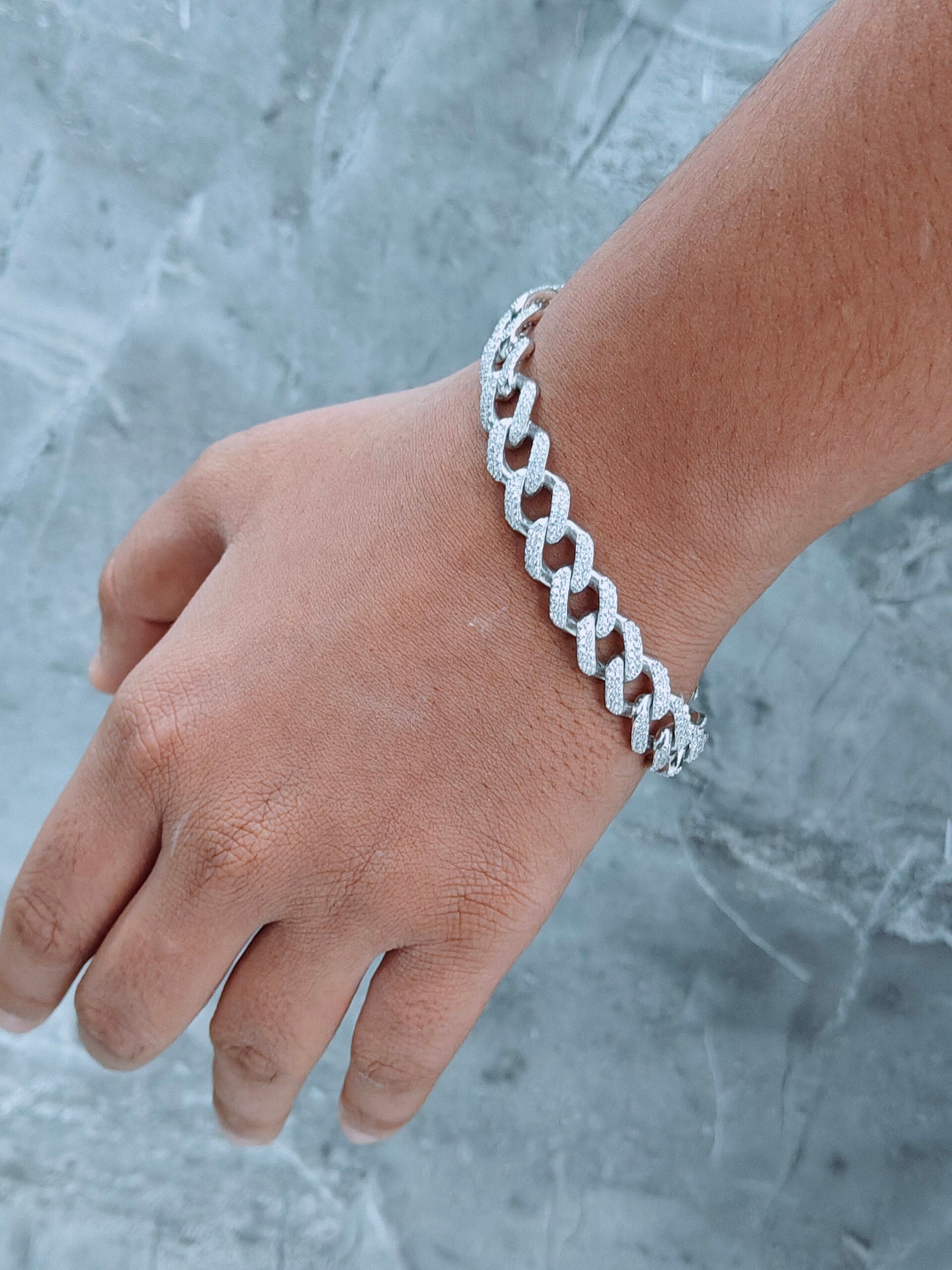 Silver chain bracelet on a wrist against a textured gray background